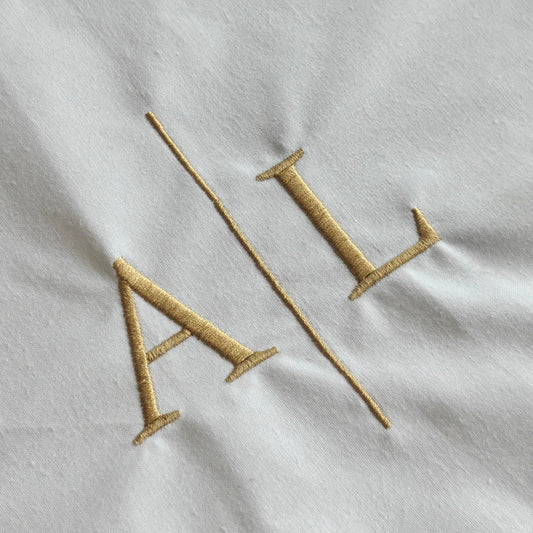 Eine Nahaufnahme der goldenen Initialen und Trennlinie Stickerei auf einem weißen Stoff.