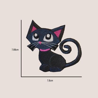Gestickter schwarzer Katzenaufnäher mit rosa Akzenten an Ohren und Halsband. Die Katze hat große weiße Augen und einen eingerollten Schwanz. Der Aufnäher misst ca. 7,66 cm x 7,6 cm.