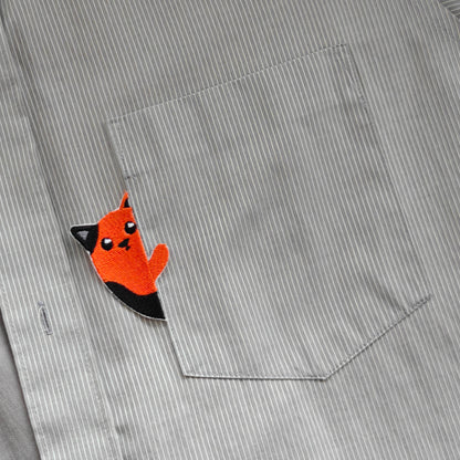 Bestickter roter Katzen-Aufnäher, der wie ein kleiner Taschengucker aus einer graugestreiften Hemdtasche hervorschaut.