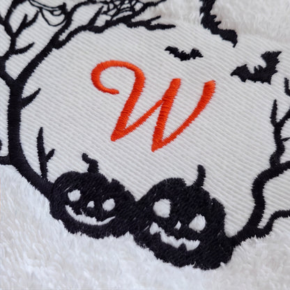 Makroaufnahme des orange gestickten Buchstaben W und der schwarzen Kürbis-Bestickung auf weißem Baumwolltuch