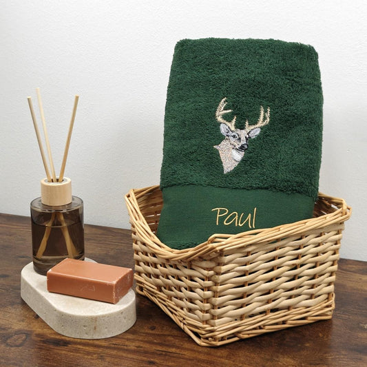 Dunkelgrünes (Bottlegreen) flauschiges Handtuch mit einer detailreichen, hellen Hirschkopf-Stickerei und dem Namen Paul in Goldschrift, präsentiert in einem hellen Weidenkorb.