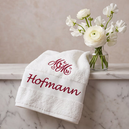 Elegantes weißes Handtuch mit weinroter Namensbestickung Hofmann auf Marmorablage neben weißer Blumenvase