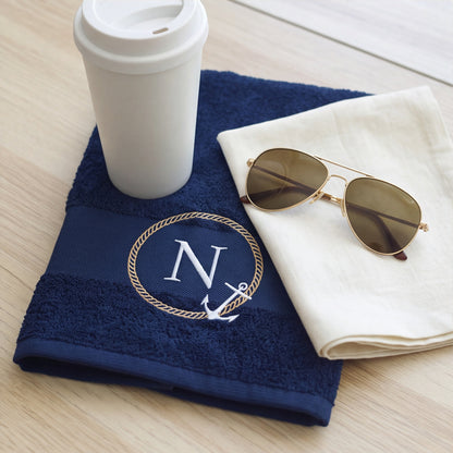 Dunkelblaues maritimes Handtuch mit Monogramm N, Kaffeebecher und Sonnenbrille auf hellem Holztisch