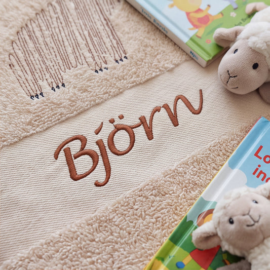 Nahaufnahme der hochwertigen braunen Namensstickerei Björn und der Bärenkontur auf dem flauschigen Baumwoll-Handtuchstoff.