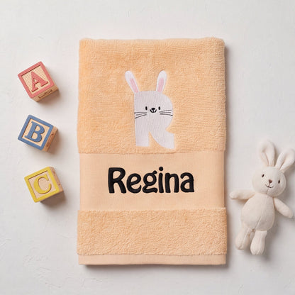 Personalisiertes Babyhandtuch mit Hasen-Buchstabe R und dem Namen Regina neben bunten ABC-Holzbausteinen und einem Kuschelhasen.
