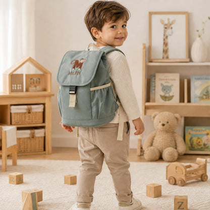 Kleiner Junge von hinten mit dem graugrünen, bestickten Rucksack Milan mit Affen-Initial M im Kinderzimmer.