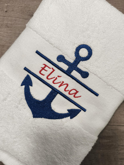 Weißes Handtuch mit einem marineblauen, gestickten Anker-Design und dem Namen "Elina" in roter Schrift. Das Handtuch ist gefaltet und zeigt die nautische Stickerei. Das Design ist auf dem Rand des Handtuchs zentriert.