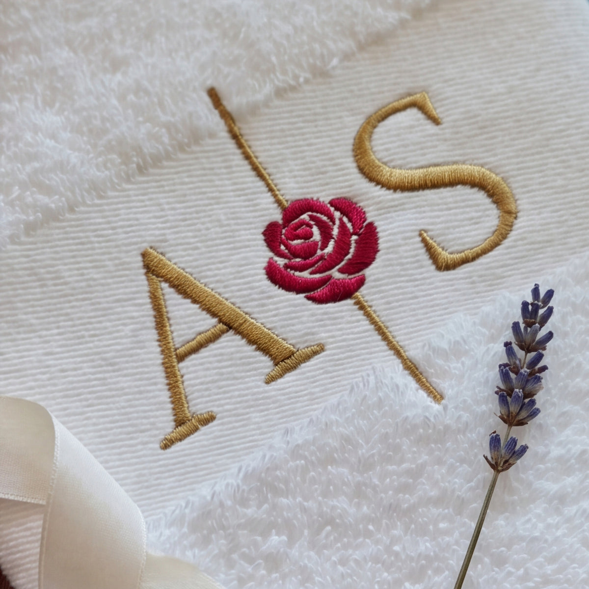 Eine Nahaufnahme der goldenen und roten Initialen und Rose Stickerei auf einem personalisierten Handtuch.